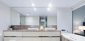 A modern bathroom with two sinks, a large mirror, a bathtub, and a vanity with cabinets. - Soul - Q Stay (Surfers Paradise)