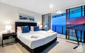 A modern hotel room with a large bed, two bedside tables, a nightstand, a framed picture, and a balcony with a view of the beach. - Soul - Q Stay (Surfers Paradise)