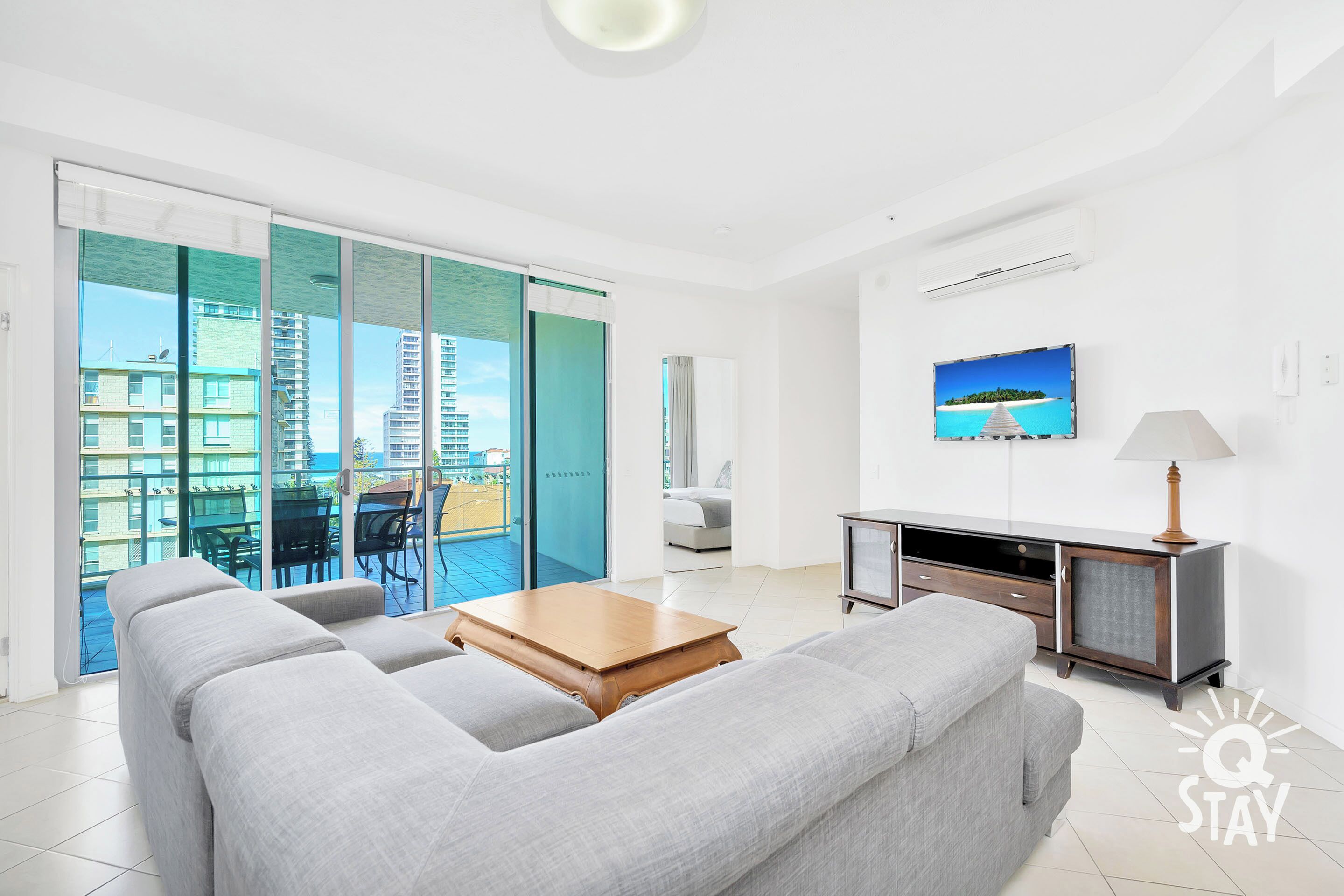 A modern living room with a grey sofa, a wooden coffee table, and a TV on the wall.