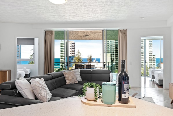 A modern living room with a dark grey sofa, a small coffee table, a potted plant, and a bottle of wine. - Wings - Q Stay (Surfers Paradise)
