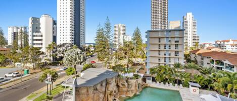 A hotel with a pool, surrounded by tall buildings and palm trees.