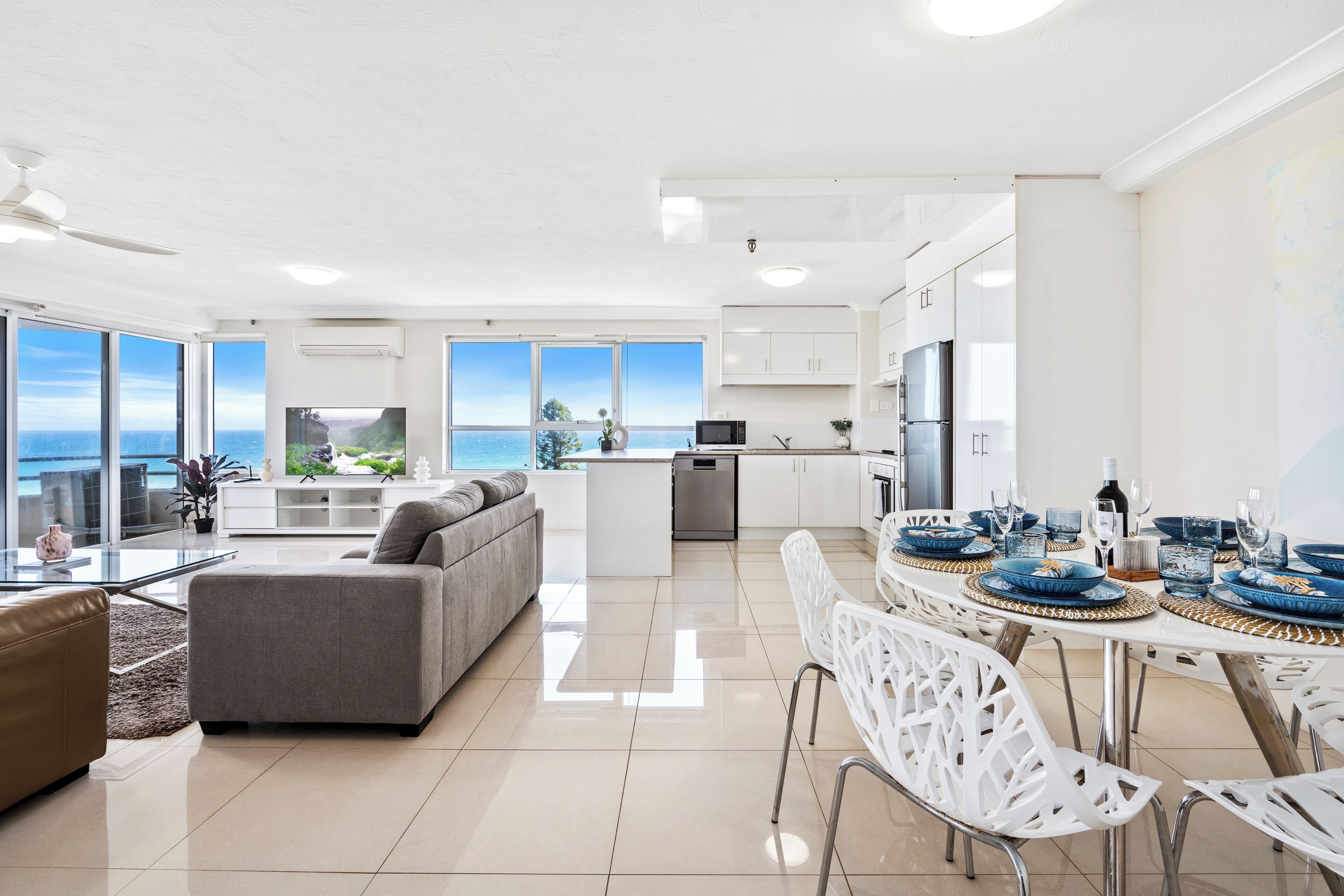 Ein modernes Wohnzimmer mit Küche, Essbereich und großen Fenstern mit Meerblick.