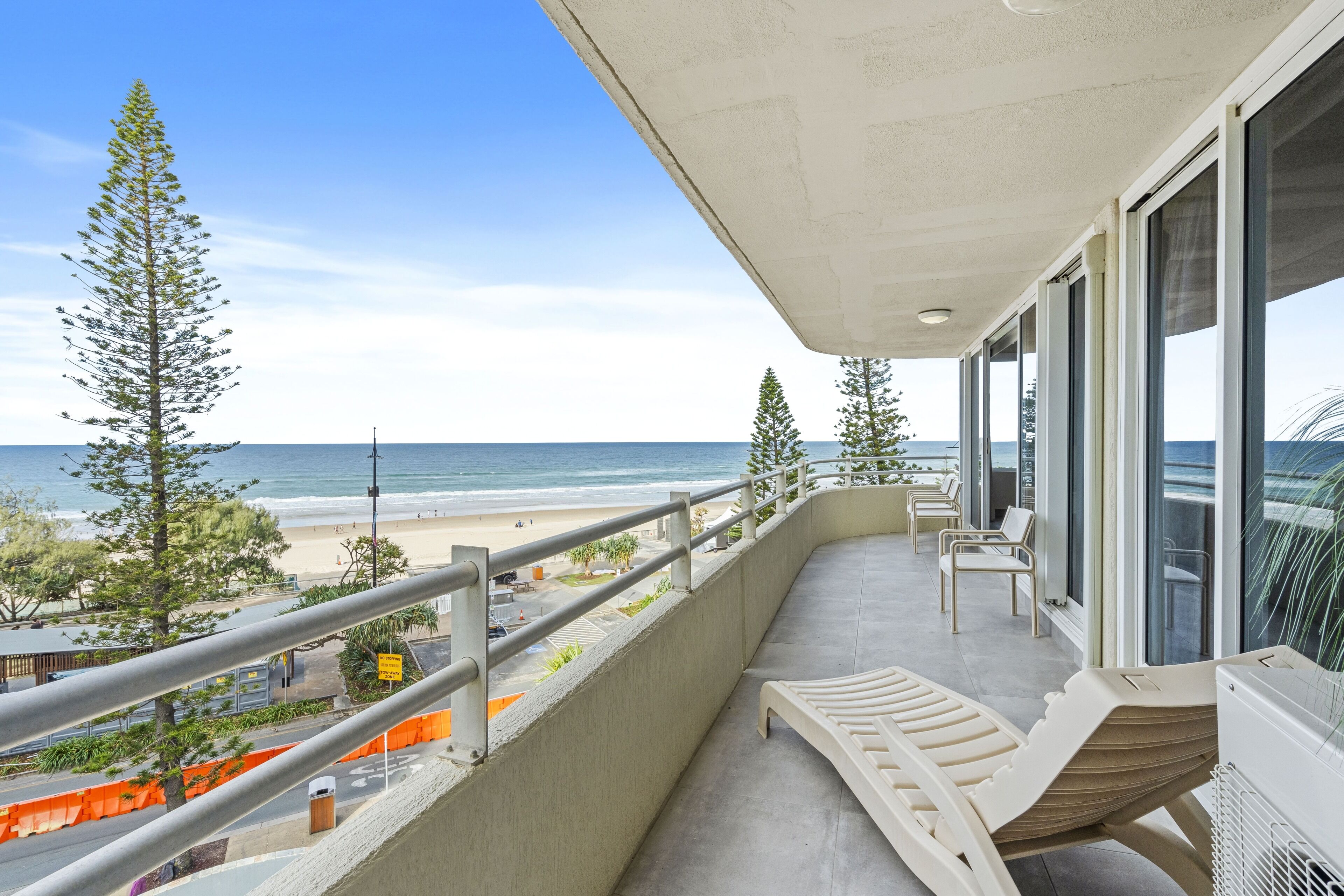 A balcony with a view of the beach, lounge chairs, and a railing.