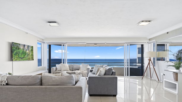 Un moderno salón con un sofá grande, un sillón más pequeño y una mesita auxiliar. La habitación tiene ventanas amplias que ofrecen vista al océano.