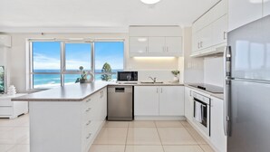 Una cocina moderna con vista al océano, muebles blancos, electrodomésticos de acero inoxidable y una isla grande.