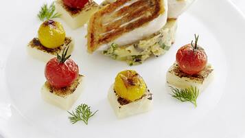A white plate with a grilled sandwich, small grilled vegetables, and a glass of white wine.