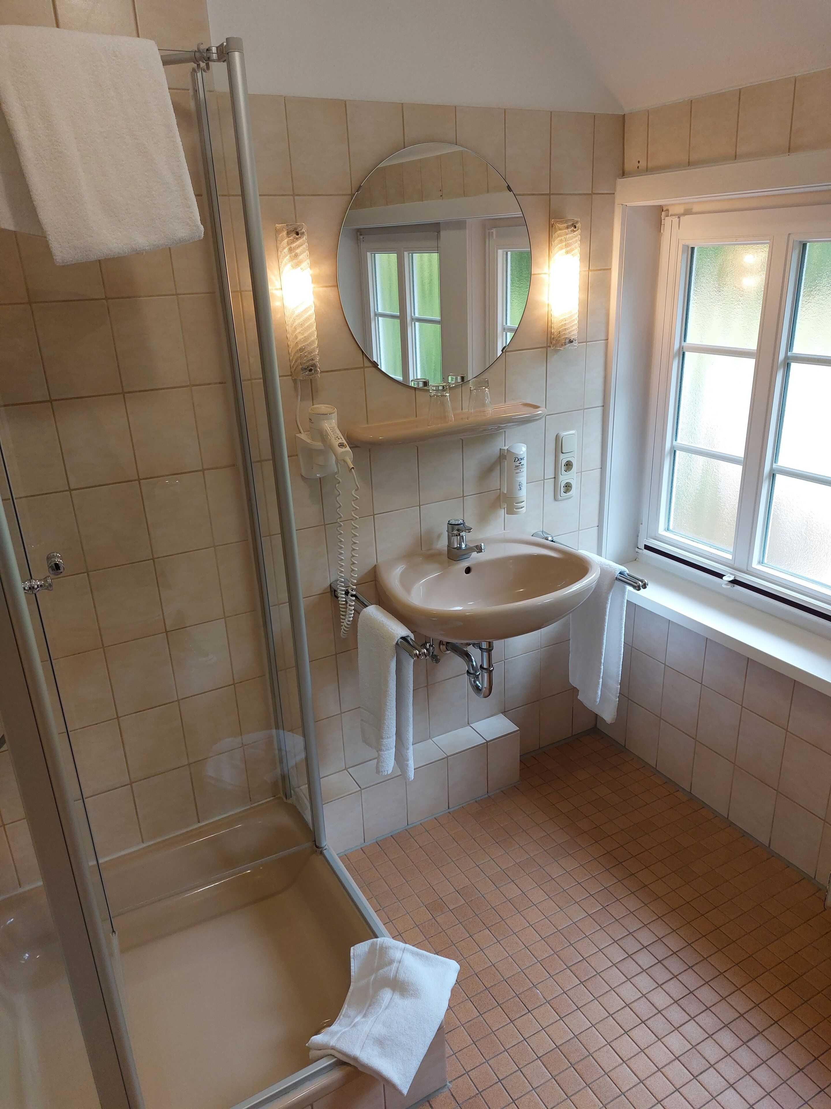 Ein Badezimmer mit Duschkabine aus Glas, Waschbecken mit Spiegel und einem Fenster für natürliches Licht.
