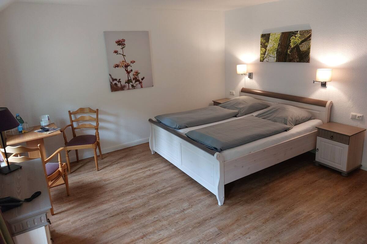 A bedroom with a bed, bedside tables, a desk with a chair, and wall-mounted lamps.