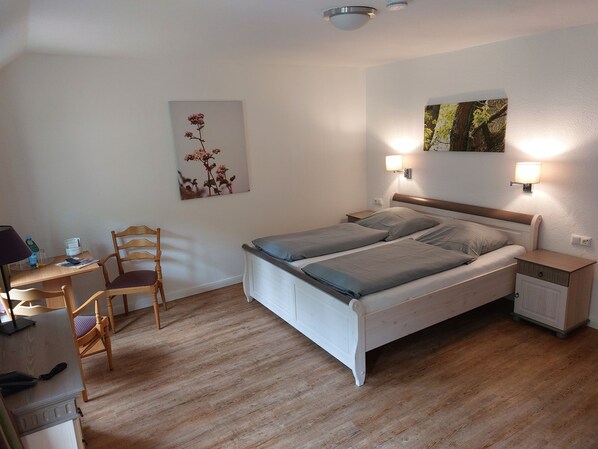 Un dormitorio con una cama, mesitas de noche, un escritorio con silla y lámparas fijadas a la pared.
