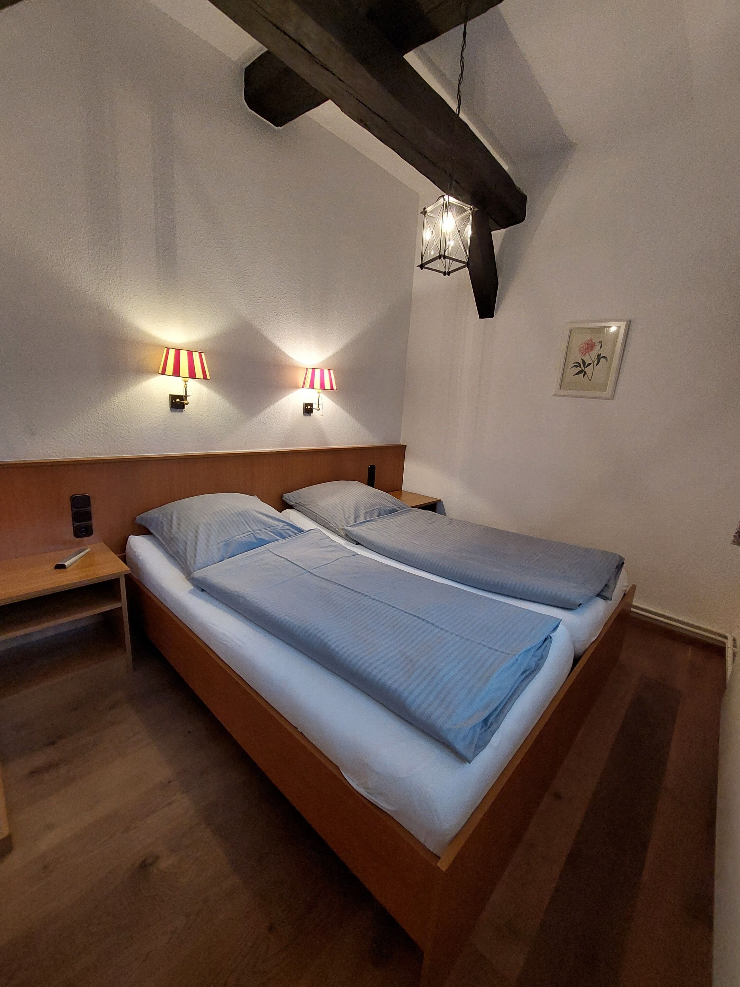 A room with two beds, wooden headboards, and two wall-mounted lamps.