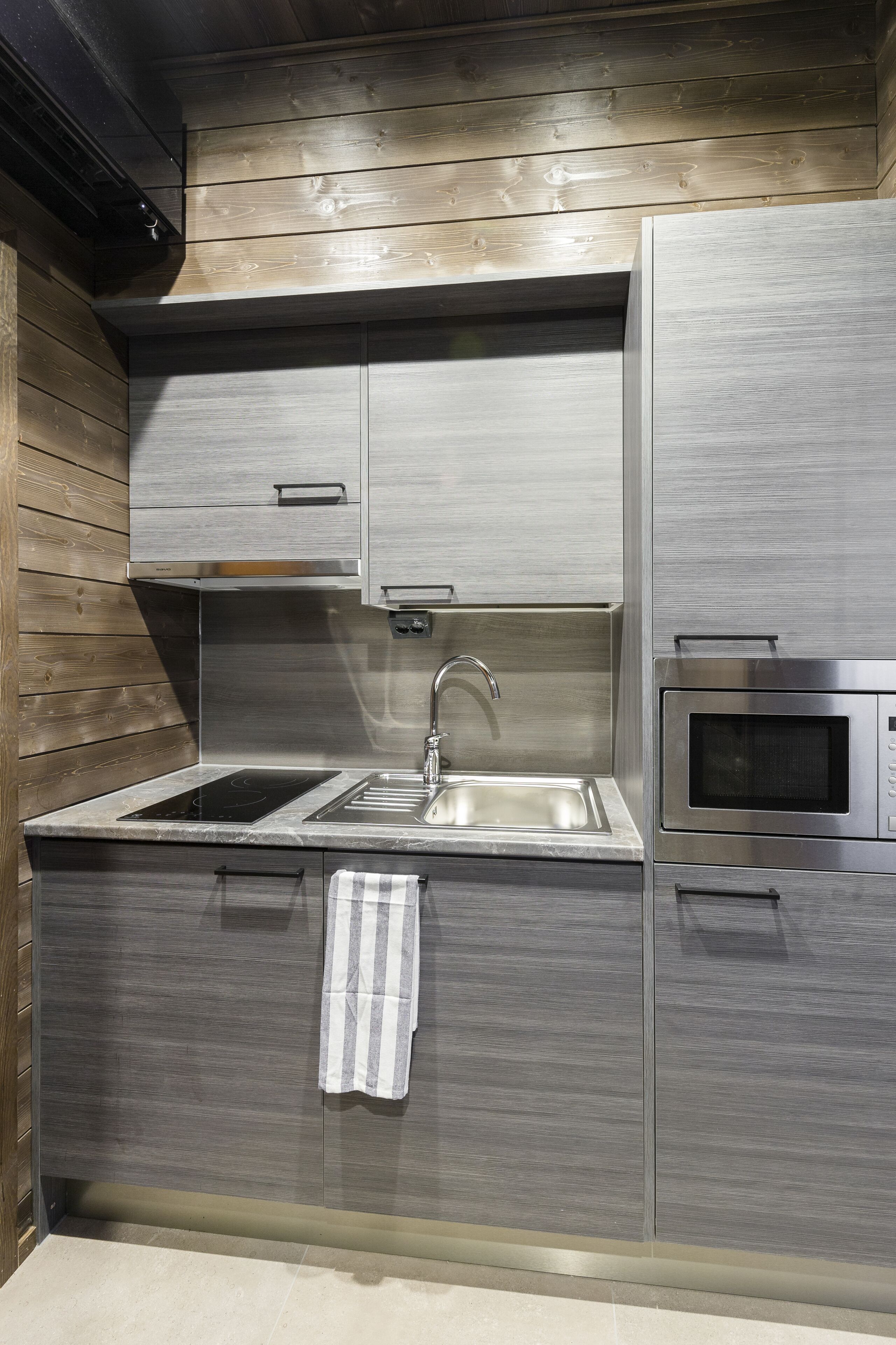 Una cocina moderna con un lavamanos de acero inoxidable, un microondas integrado y paneles de madera en los armarios superiores.