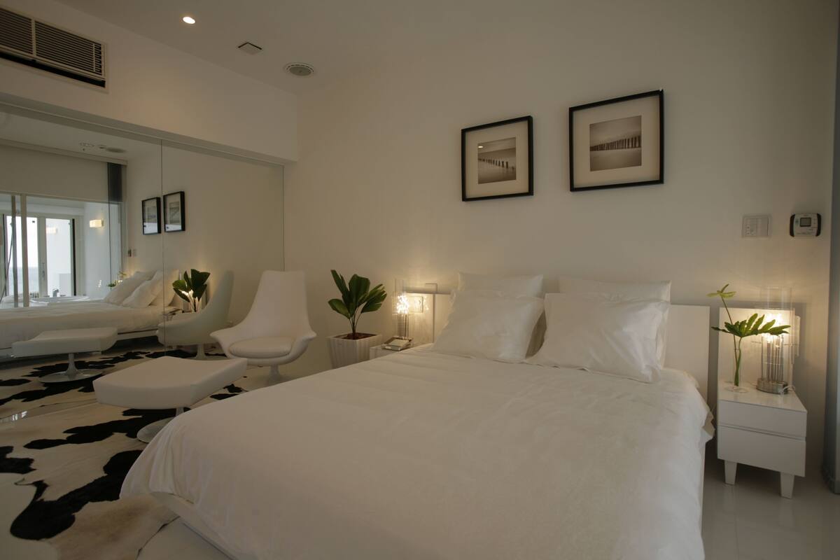 A modern bedroom with a large bed, two chairs, a small table, and a nightstand.