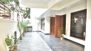 A corridor with tiled flooring, potted plants, wooden doors, and a window. - The Country Roads (New Delhi)