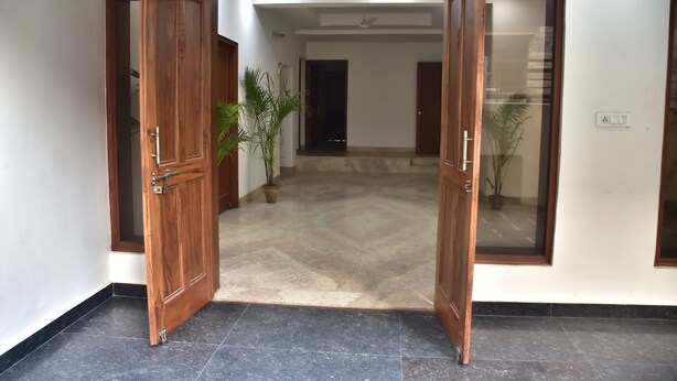 An open wooden door leading to a tiled hallway with potted plants. - The Country Roads (New Delhi)