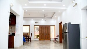 A spacious kitchen with a refrigerator, wooden cabinets, and a dining area with chairs and a table. - The Country Roads (New Delhi)