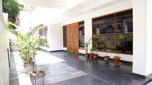 A clean, well-maintained indoor corridor with potted plants, a wooden door, and a tiled floor. - The Country Roads (New Delhi)