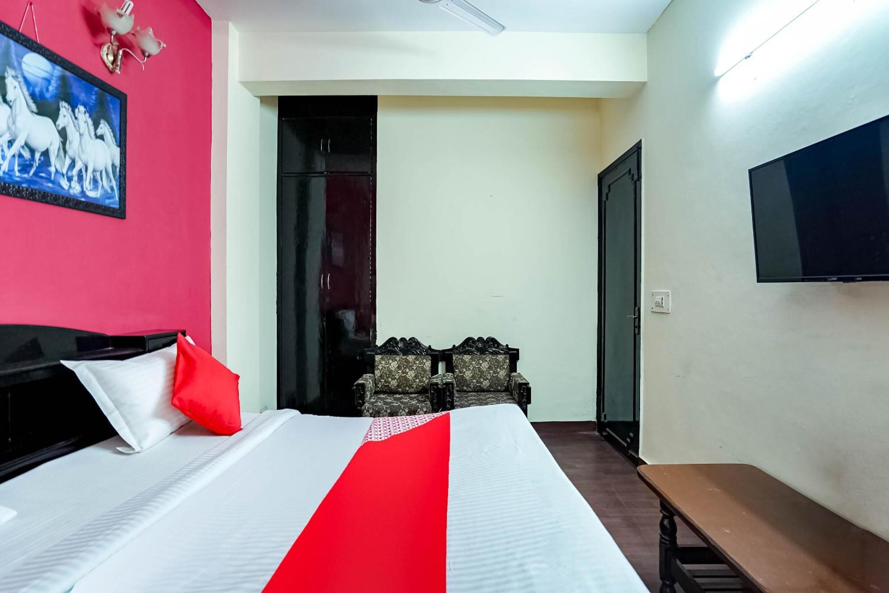 A hotel room with a bed, a TV, a bench, and a door leading to another room.