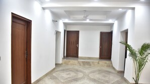 A hallway with two wooden doors, a ceiling fan, and a potted plant. - The Country Roads (New Delhi)