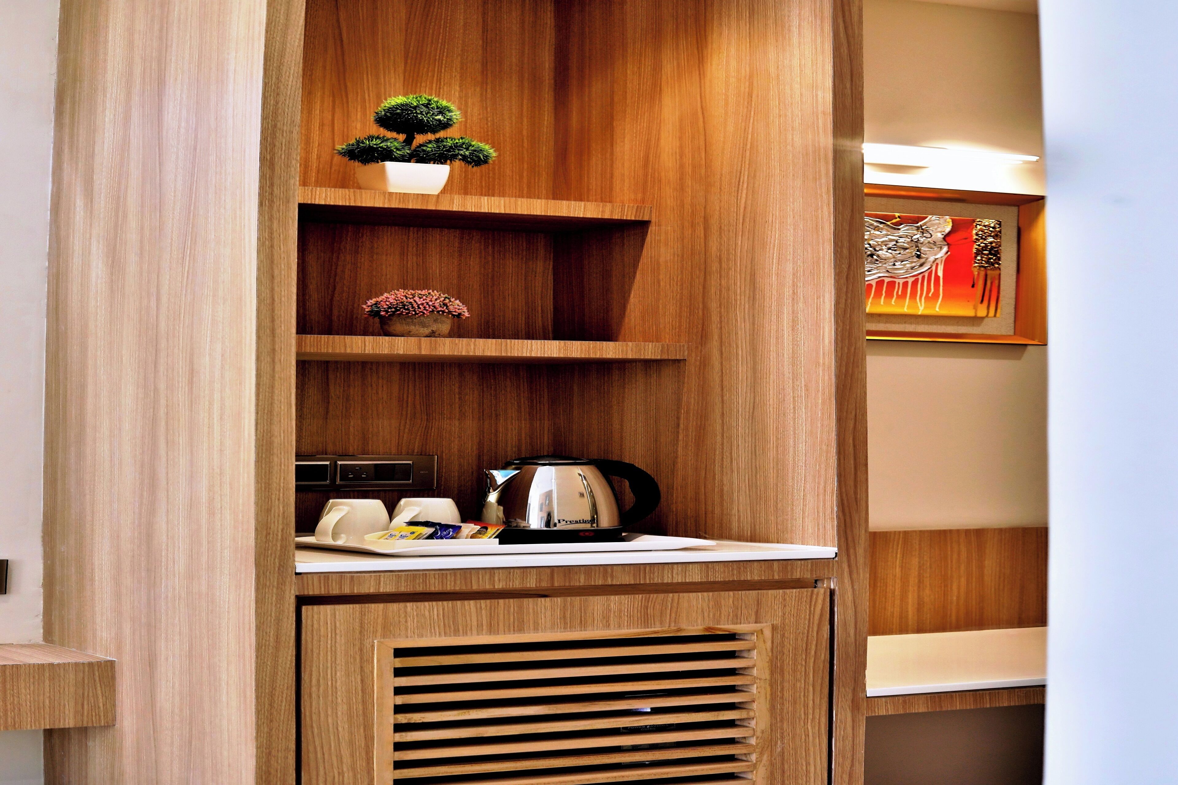 A wooden cabinet with a coffee maker, a small potted plant, and a framed artwork.