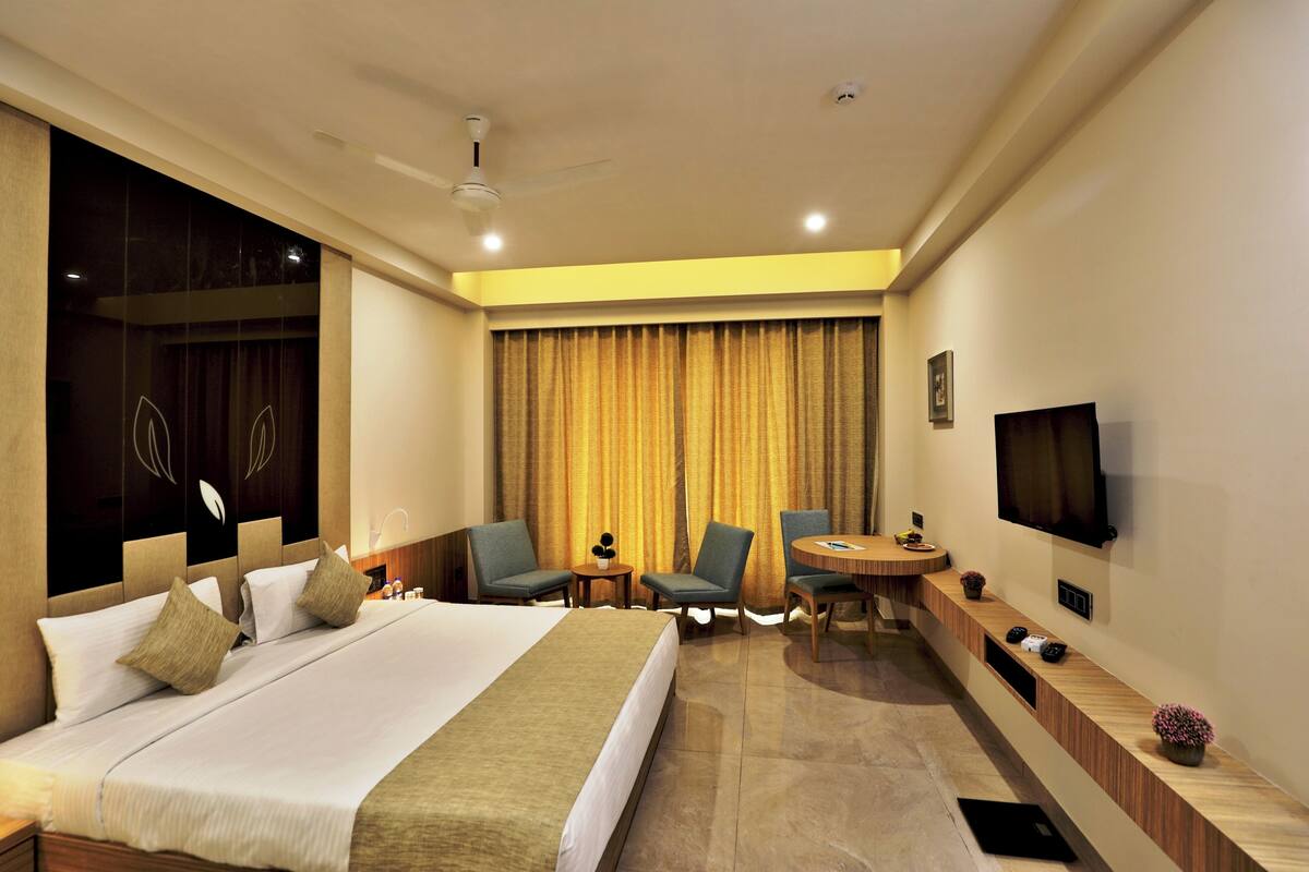 A hotel room with a large bed, two armchairs, a small table, a TV, and a ceiling fan.