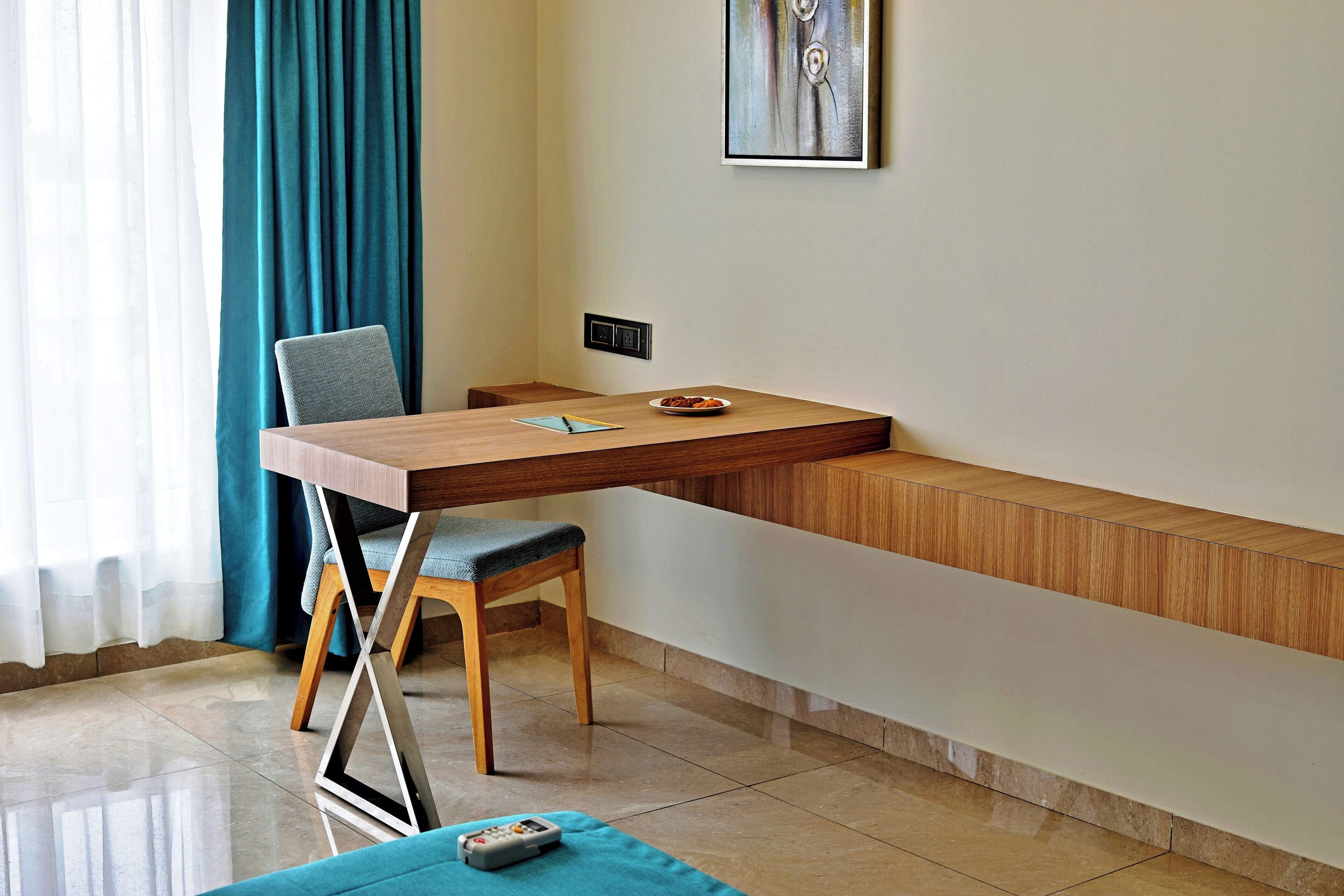 Una habitación moderna con un escritorio de madera, una silla, una mesita con un plato y un control remoto sobre una alfombra azul.