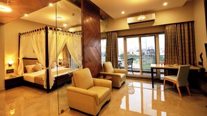 A bedroom with a four-poster bed, a sitting area with chairs, a dining table, and a balcony with a view. - VITS Devbhumi, Dwarka (Dwarka)