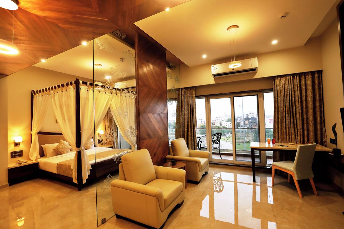 A bedroom with a four-poster bed, a sitting area with chairs, a dining table, and a balcony with a view.