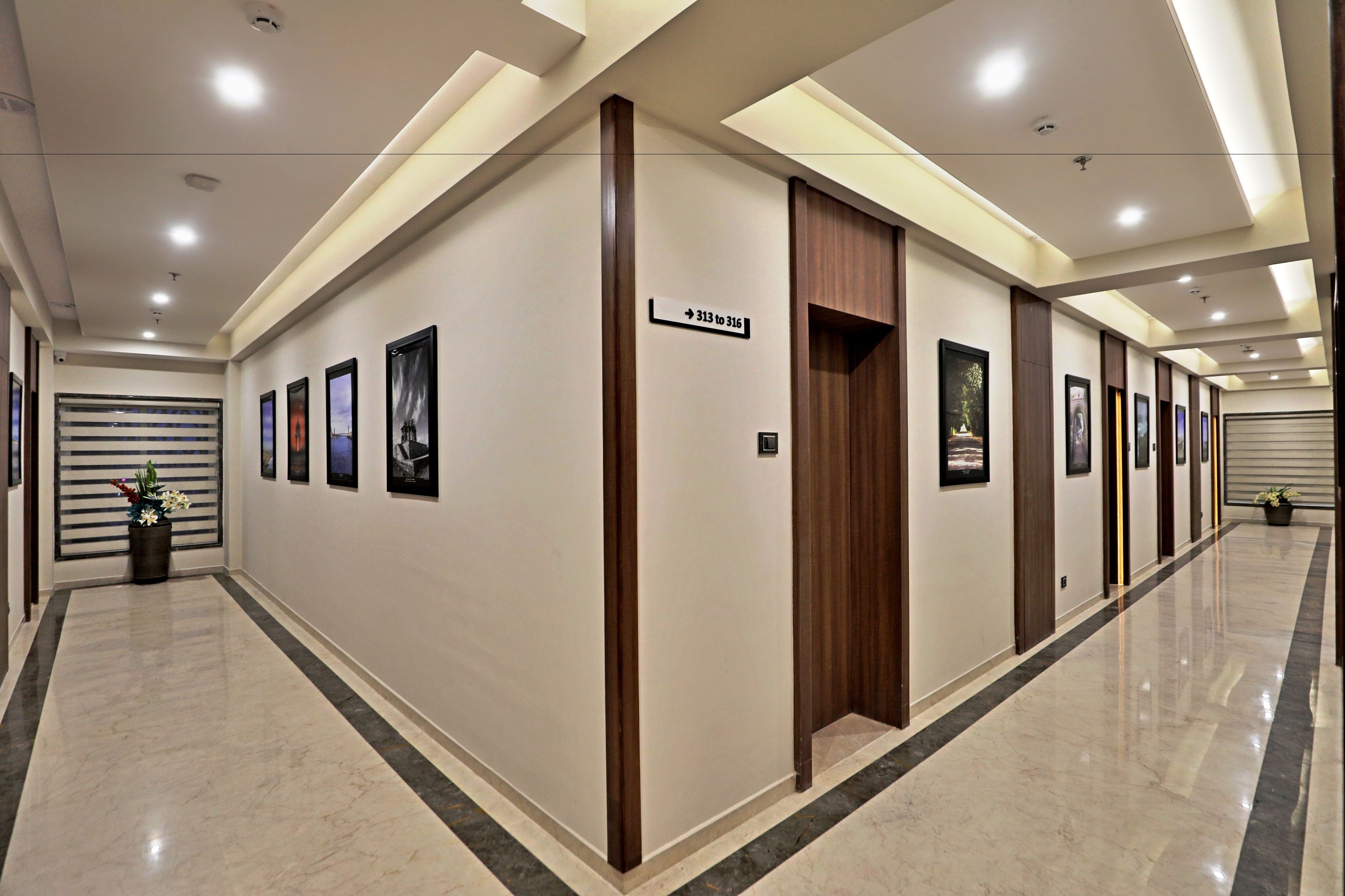 A hallway with a polished marble floor, framed artwork on the walls, and a wooden door with a sign above it.