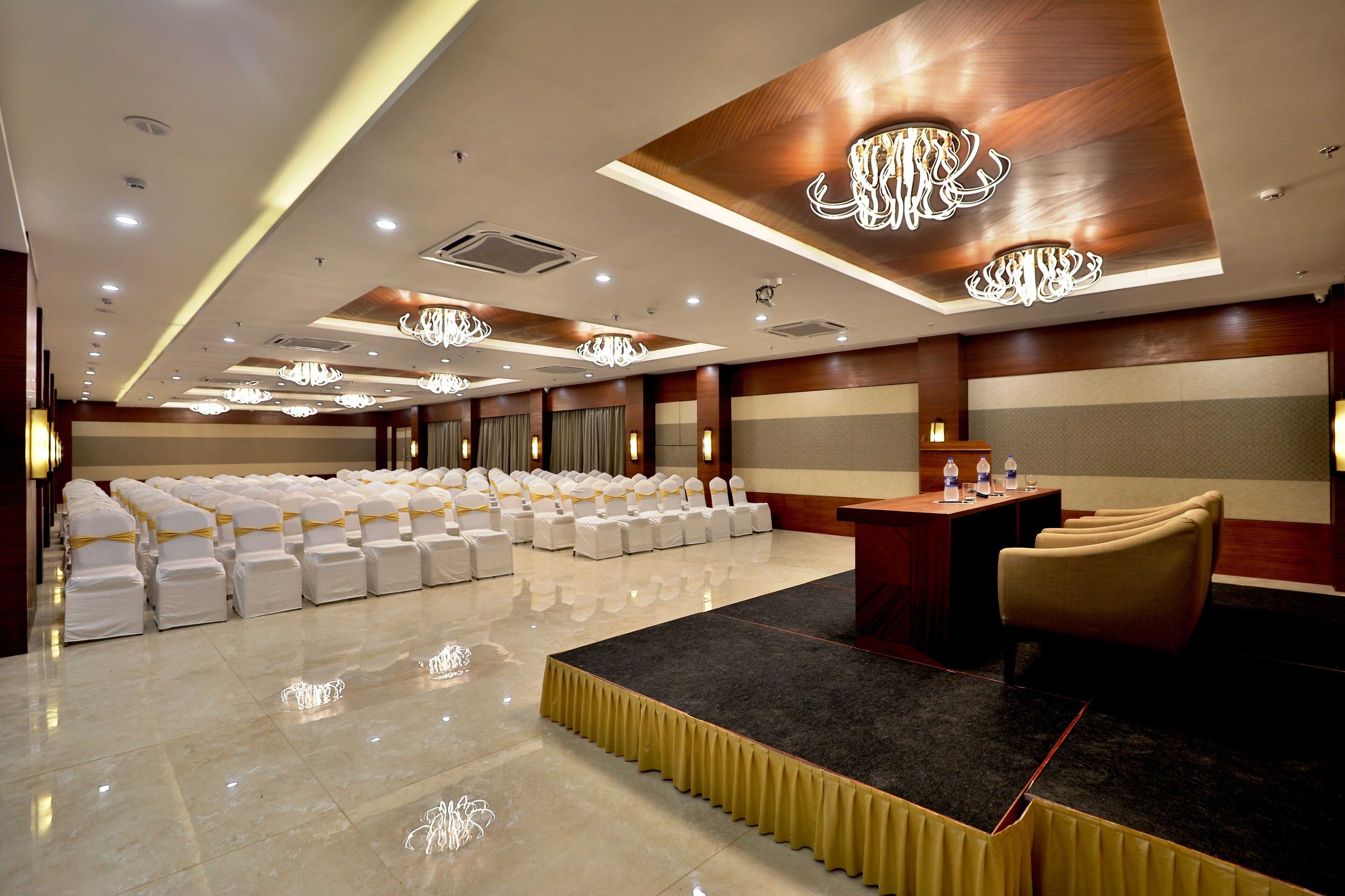 A conference room with rows of white chairs, a podium, and chandeliers.