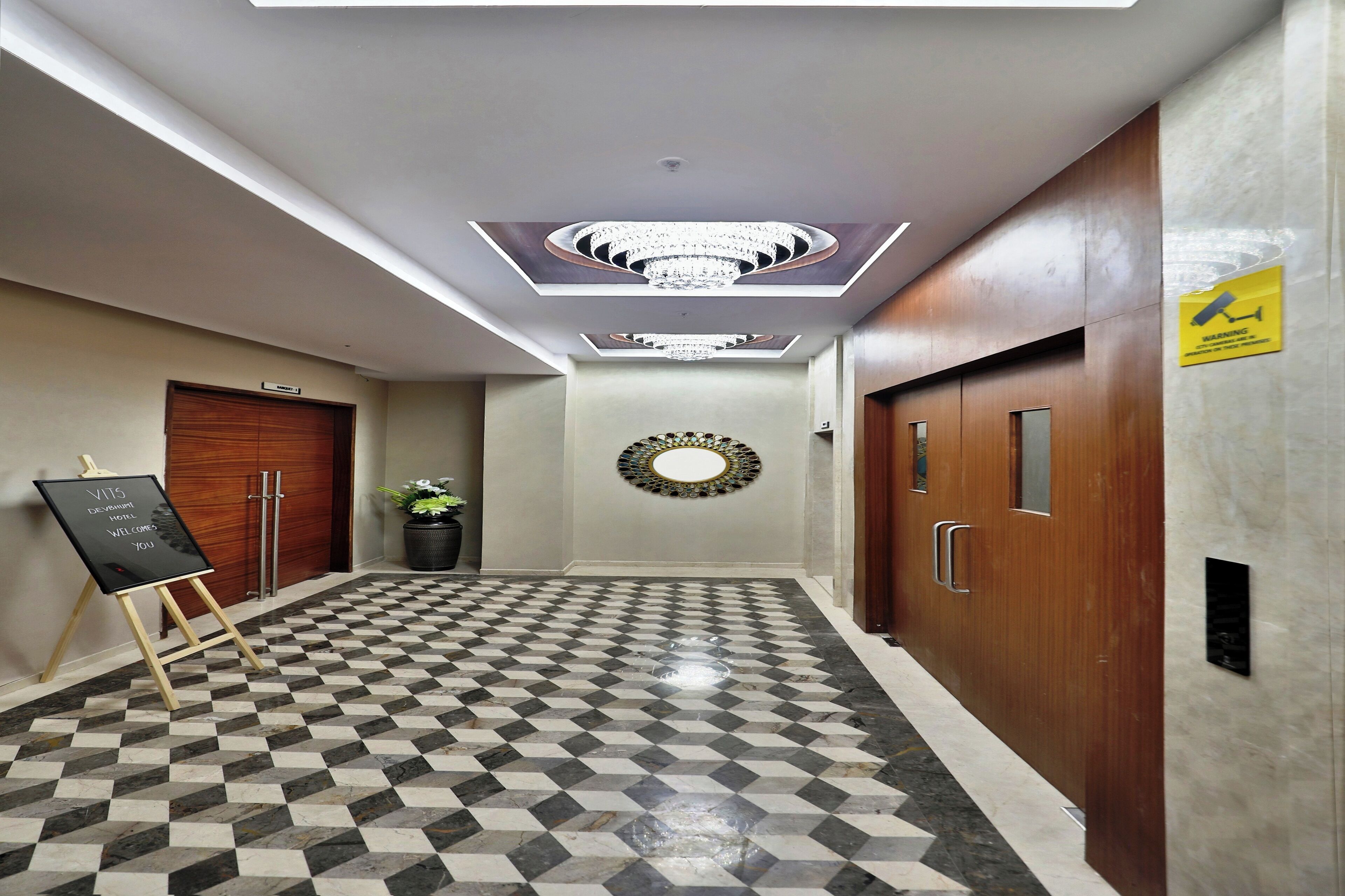 A hotel lobby with a checkered floor, a chandelier, a welcome sign, and a warning sign.