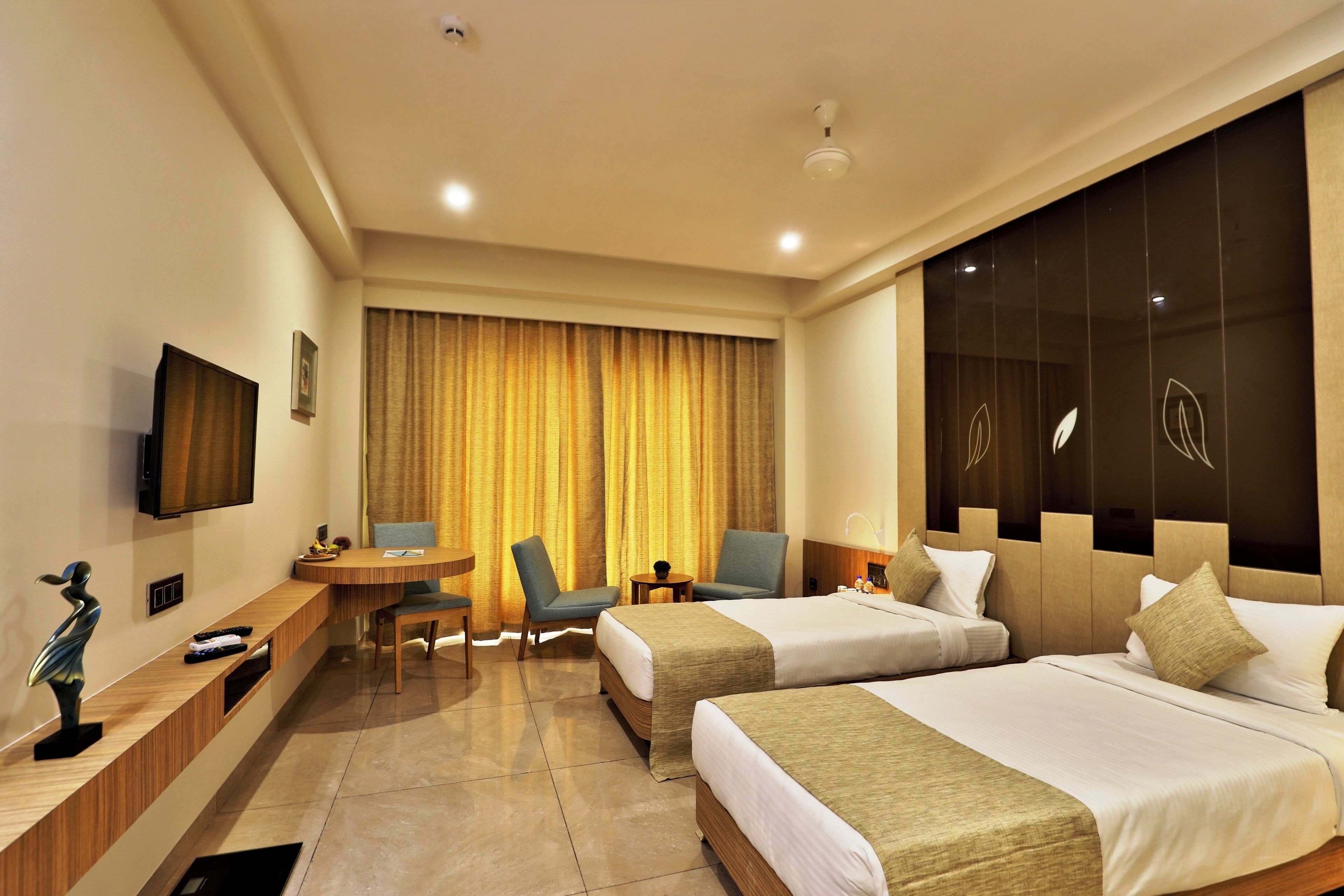 A hotel room with two beds, a desk with a chair, a TV, and a large window with curtains.