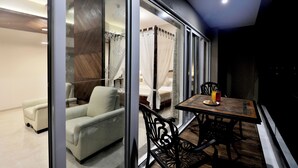 A modern bedroom with a glass door, a bed with white curtains, a sitting area with a sofa and chairs, and a dining table with a plate and a glass of juice. - VITS Devbhumi, Dwarka (Dwarka)