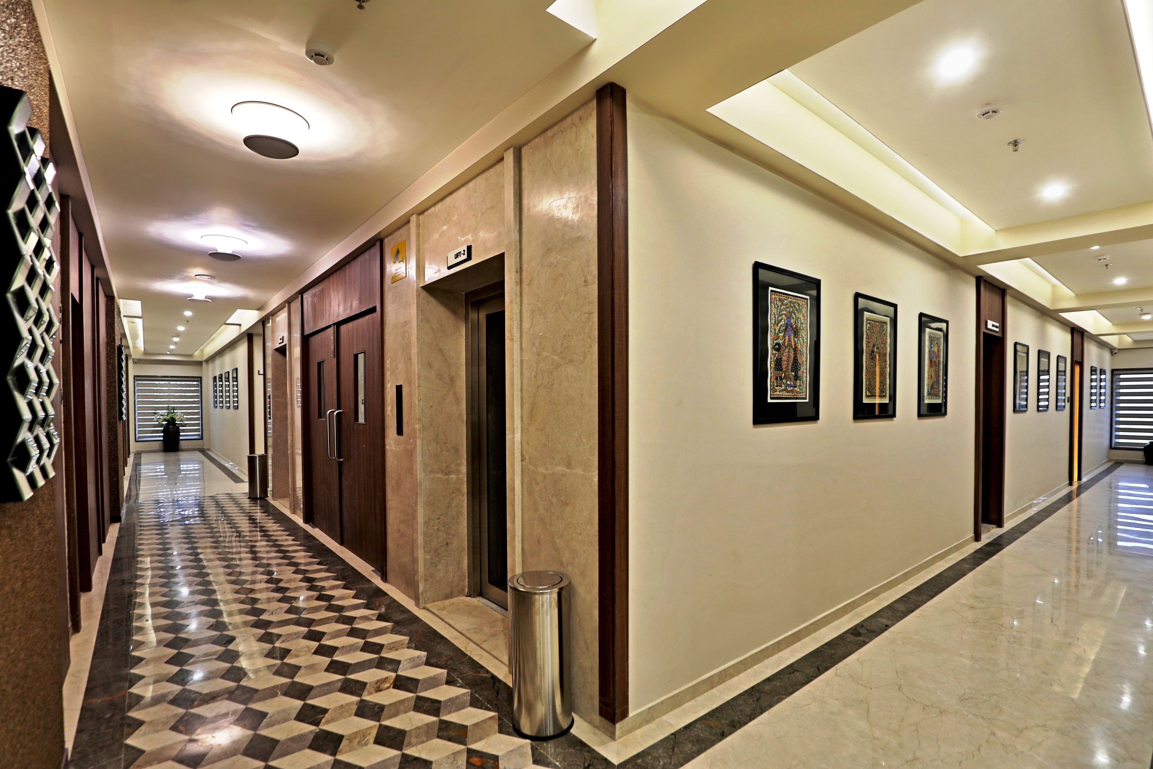 A hotel corridor with a checkered floor, wooden doors, and framed artwork on the walls.