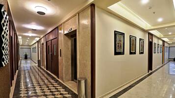 A hotel corridor with a checkered floor, wooden doors, and framed artwork on the walls.