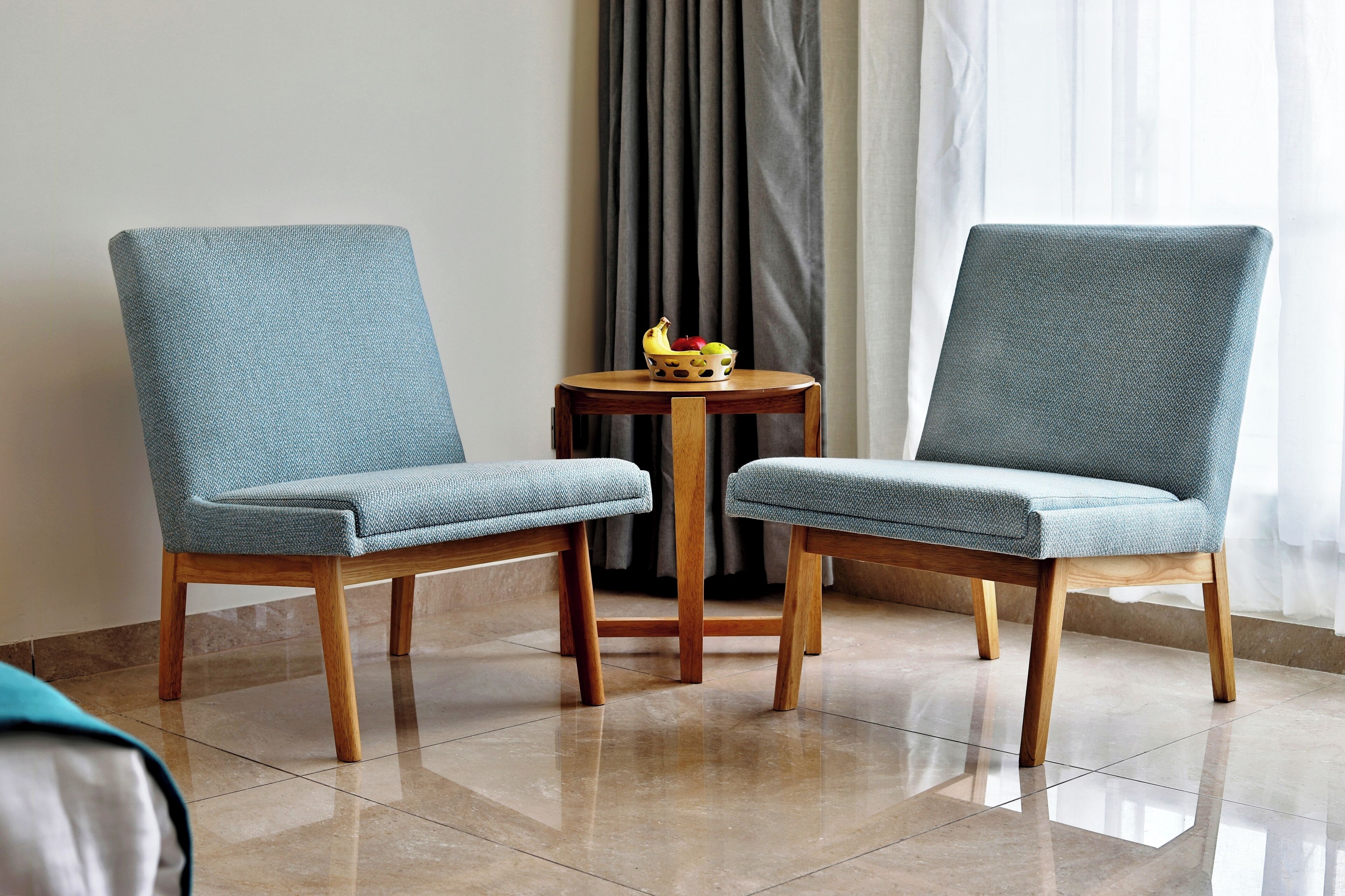 Deux chaises assorties, avec des pieds en bois, et une petite table ronde, entre lesquelles se trouve un saladier rempli de fruits.