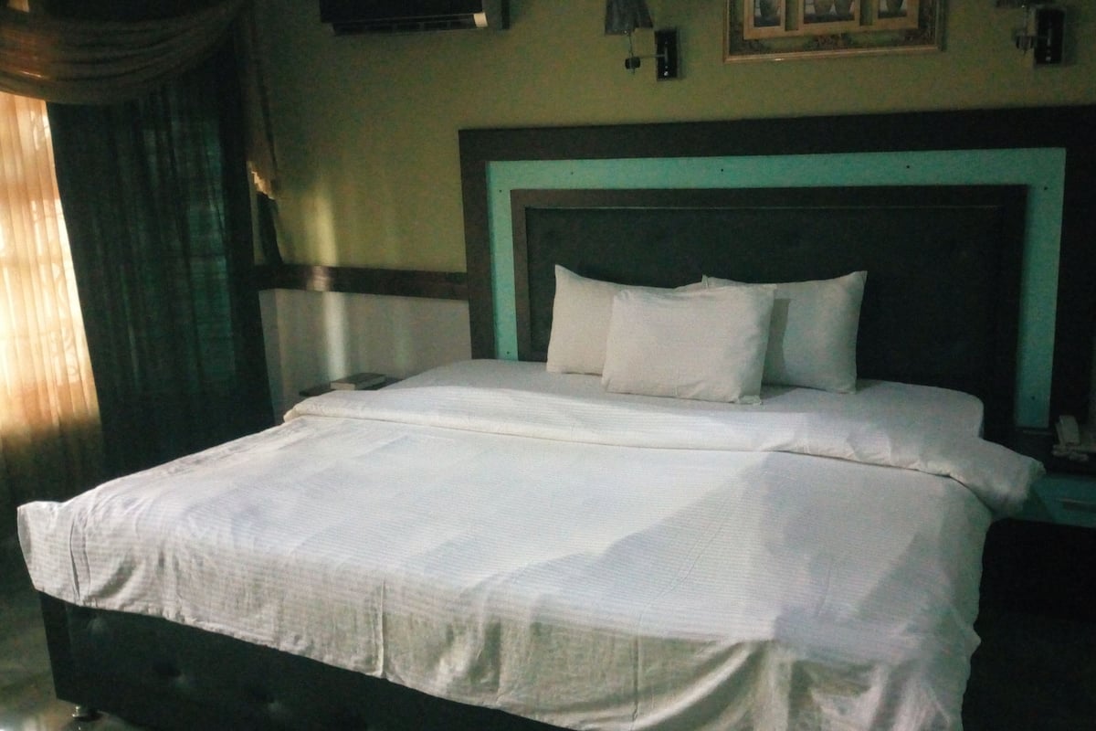 Een net opgemaakt bed met witte lakens in een kamer met een donker hoofdbord en lichte wanden.