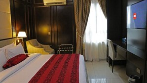 Ein Hotelzimmer mit Bett, Schreibtisch, Sessel, Klimaanlage und Fernseher.