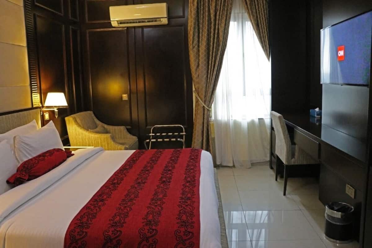 Een hotelkamer met een bed, een bureau, een stoel, een airconditioner en een televisie.