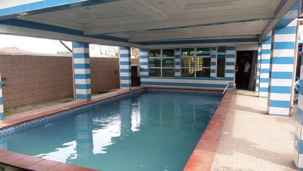 Ein Swimmingpool mit Fliesenveranda und überdachtem Bereich mit blau-weiß gestreiften Wänden.