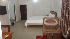 A hotel room with a bed, a chair, a TV, and a door. - Chinox Guest Inn (Abuja)