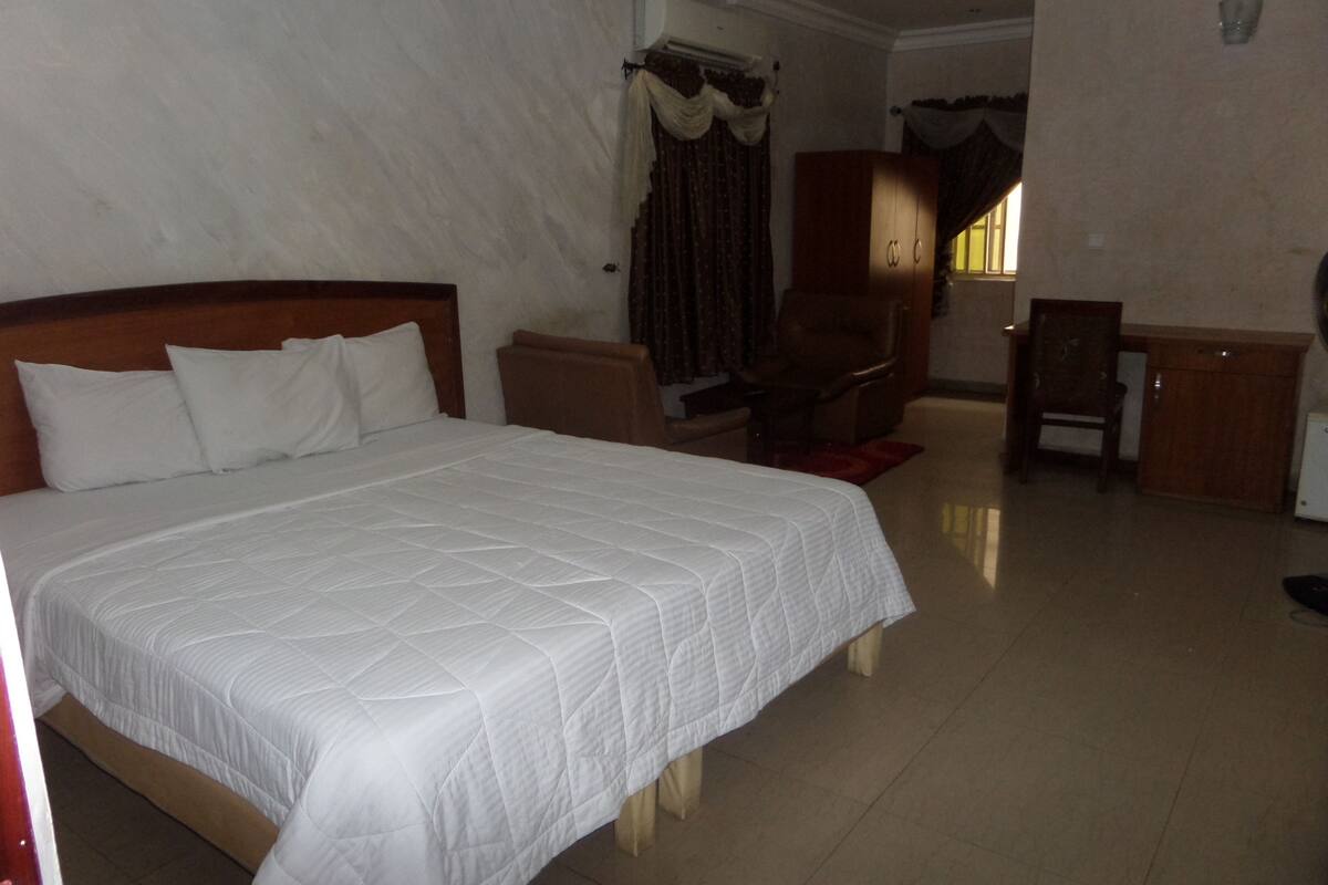 A hotel room with a large bed, a desk, a chair, and a wardrobe.