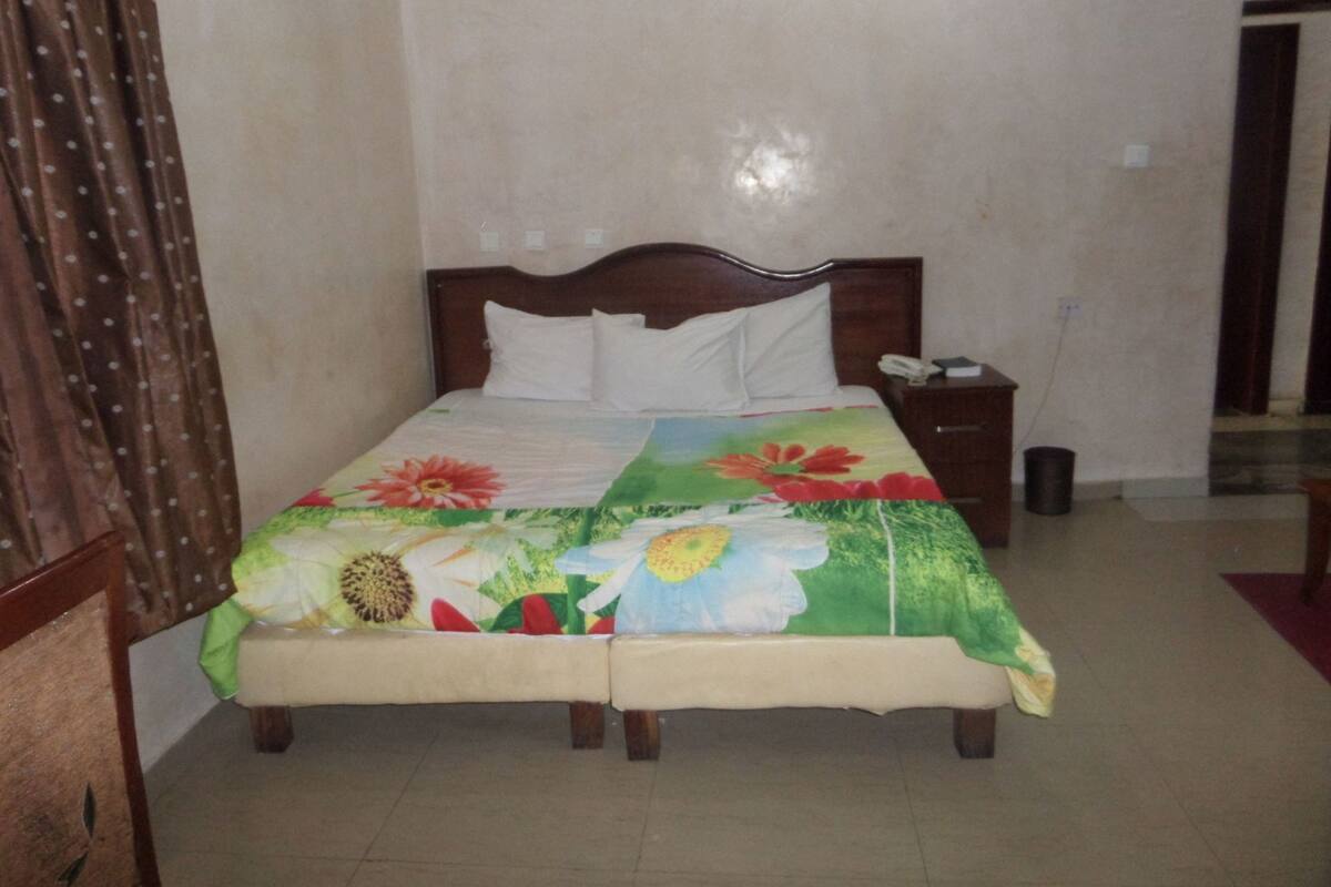 A single bed with a floral bedspread, a wooden headboard, a bedside table with a phone, and a nightstand with a trash can.