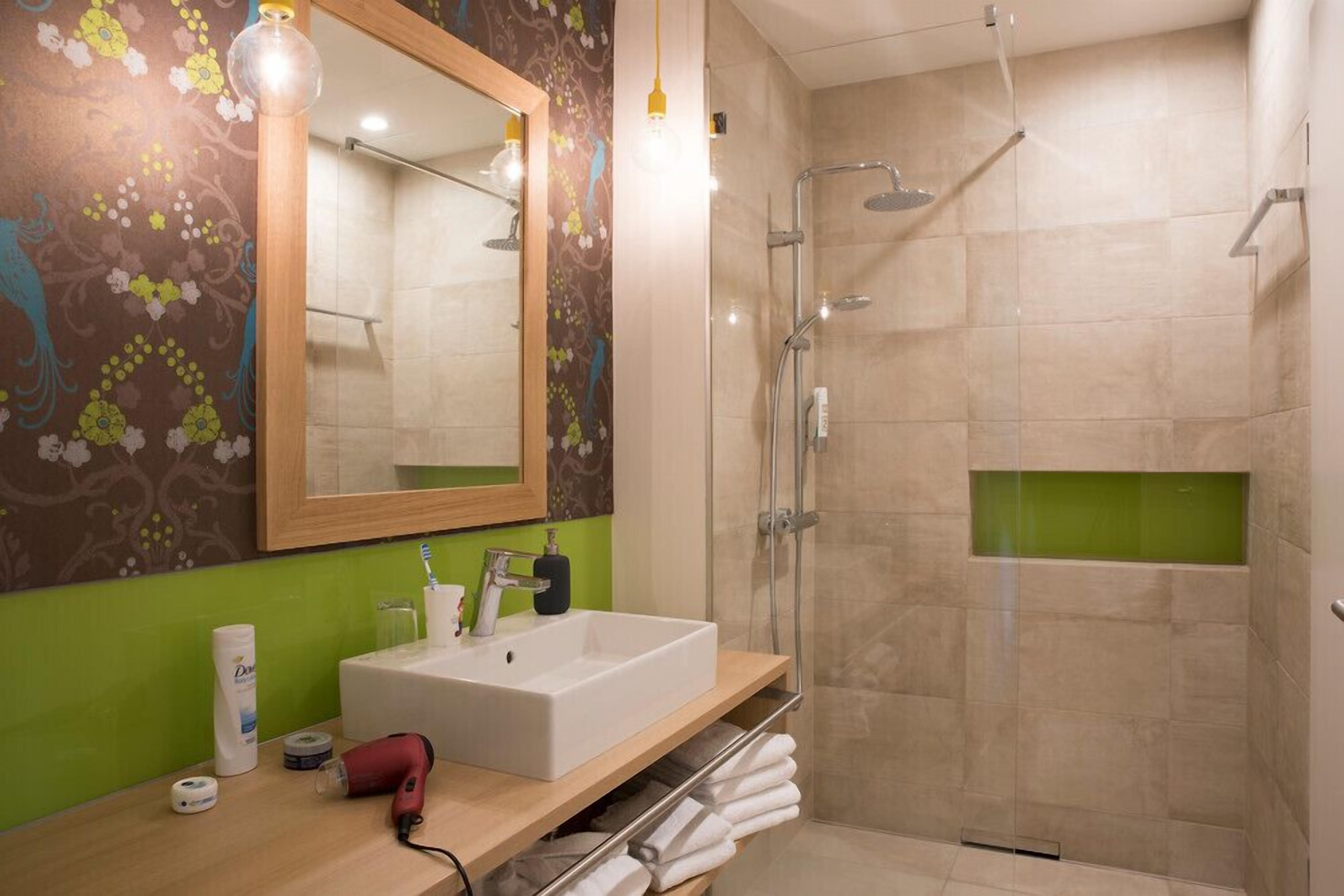 A modern bathroom with a large mirror, a white sink, a shower, and a towel rack.