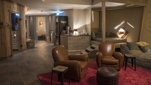 Un salon moderne avec des fauteuils en cuir, un tapis rouge et un coin cuisine comprenant un réfrigérateur et une machine à café.