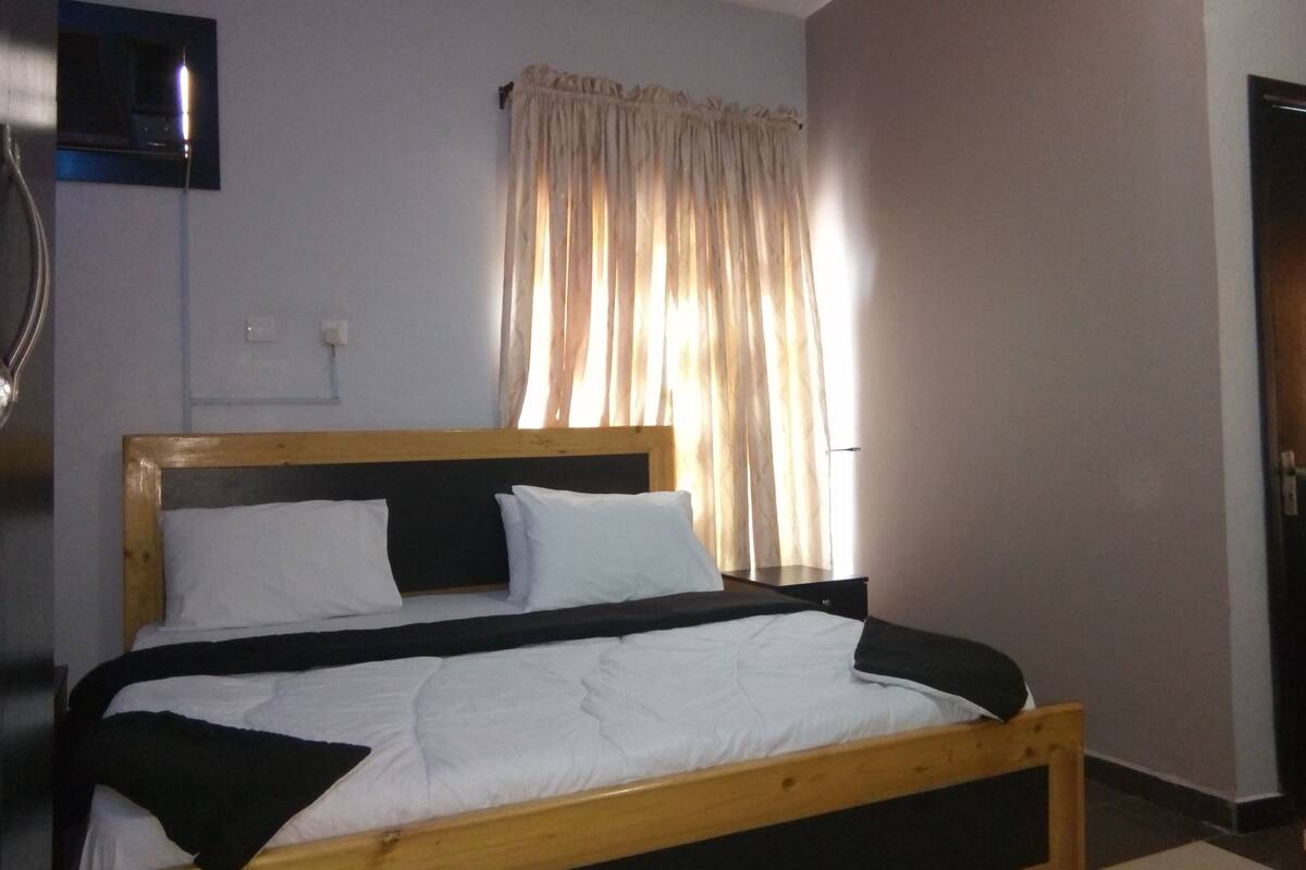 A single bed with white bedding, a wooden headboard, and a window with sheer curtains.