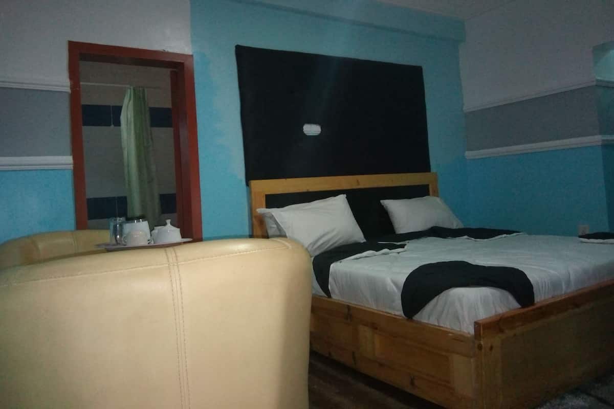 A bedroom with a bed, a wooden headboard, a bedside table with a lamp, and a chair.