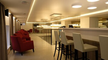 A modern hotel lobby with a bar area, red seating, and a glass partition.