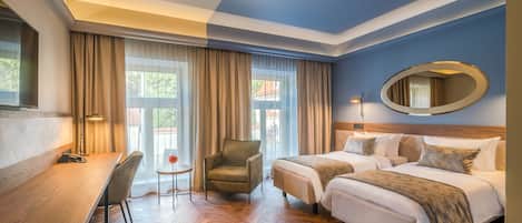 A hotel room with a wooden desk, two beds, a chair, and a large mirror.