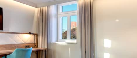 A hotel room with a bed, a desk, a chair, and a window with curtains.