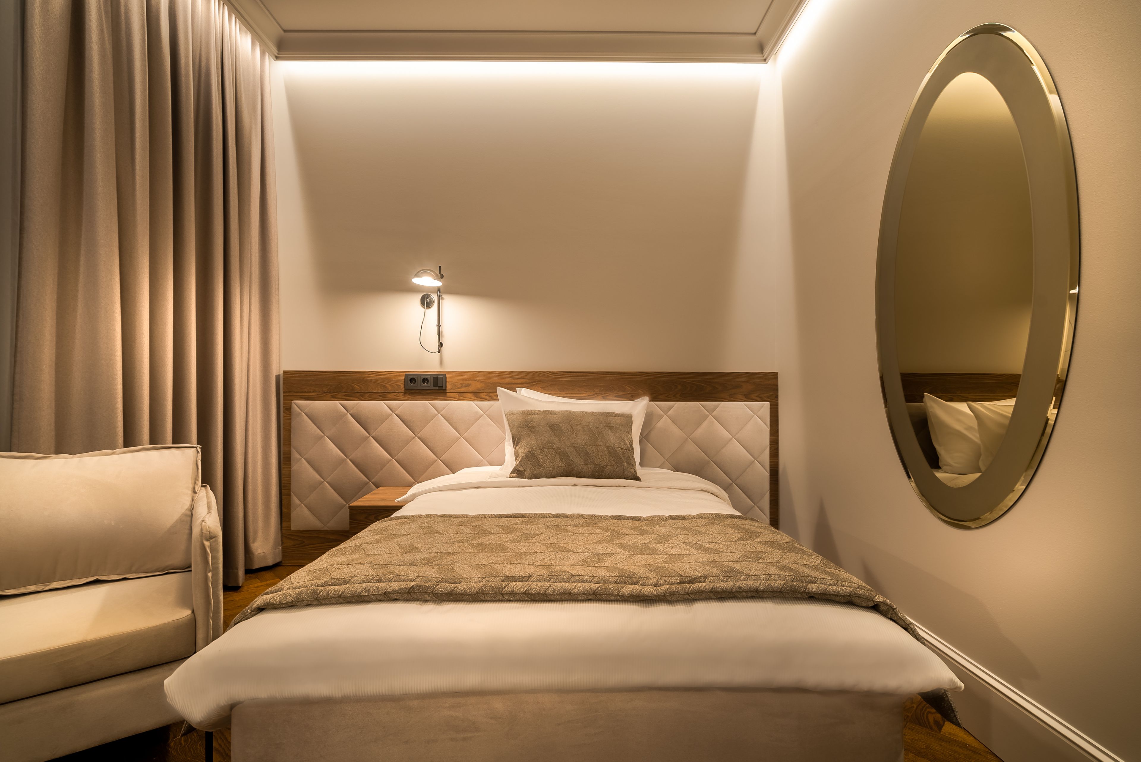 A hotel room with a bed, a nightstand, a lamp, a mirror, and a sofa.